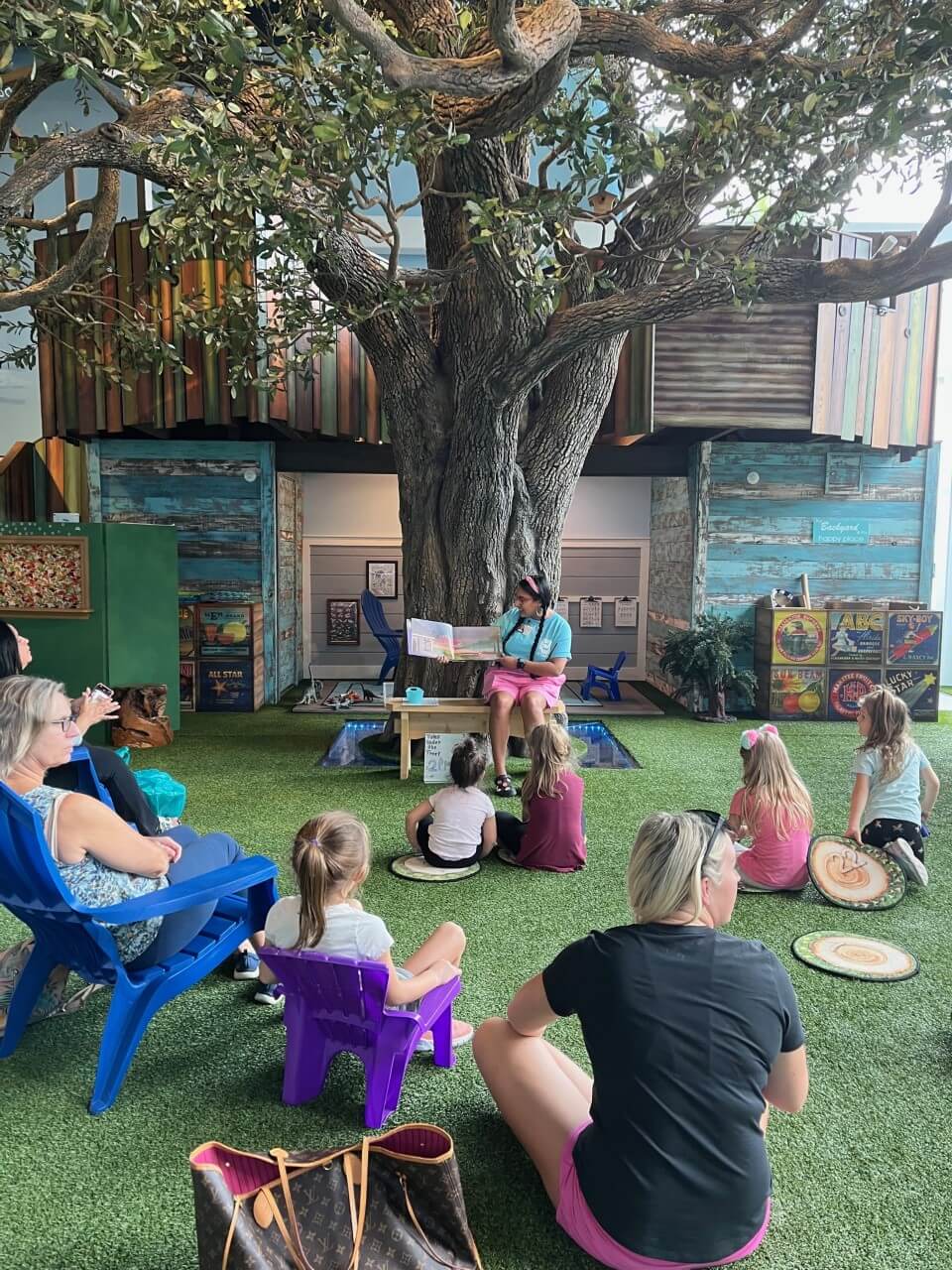 Image of a group of children and adults listening to someone read a book aloud for the Tales Under the Tree program at the Bishop Museum of Science and Nature.