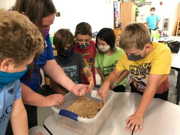 Image of an adult and a group of children surrounding a plastic tub for a science project.