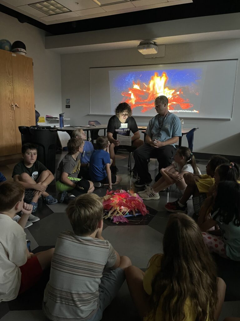 Camp Counselors read a story about mysterious creatures to a group of campers.
